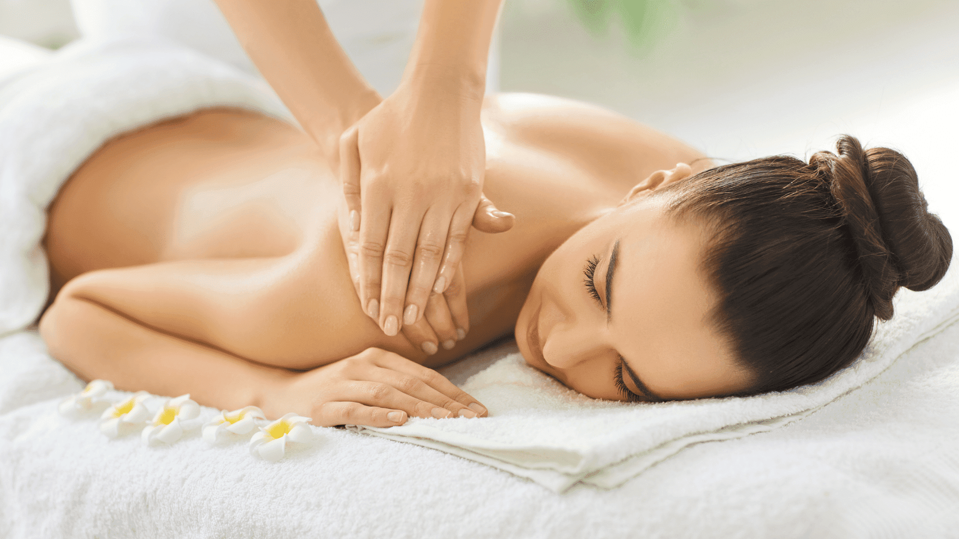 Woman receiving a relaxing back massage with flower petals beside her.
